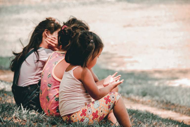 three girls sitting together on grass