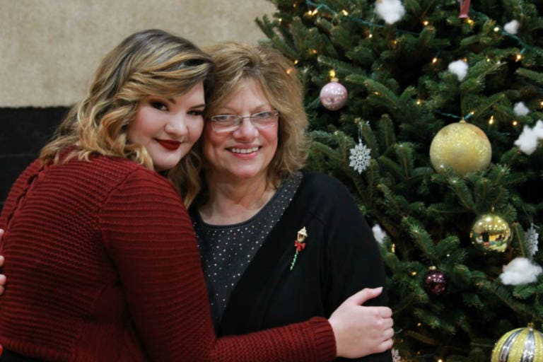 adult and a teen hugging in front of a christmas tree