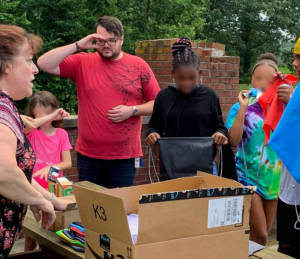 middle aged woman handing out cinch bags to teen kids from behind a table