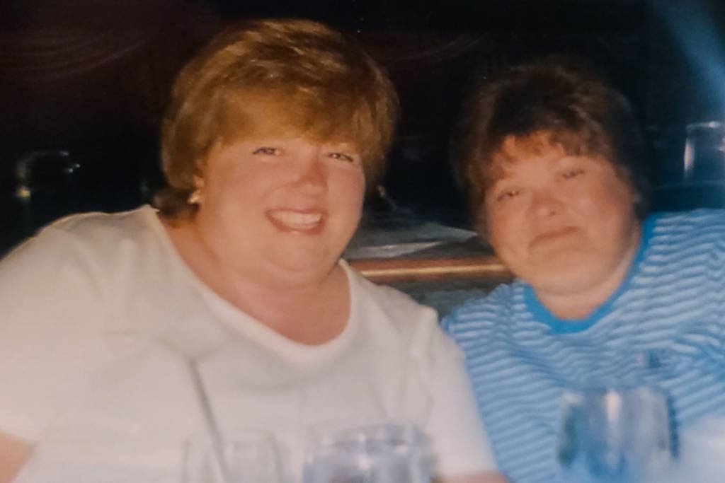 two women with short haircuts in t-shirts sitting in a booth at a restaurant smiling