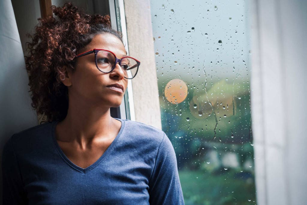 Portrait of pensive black woman standing beside window