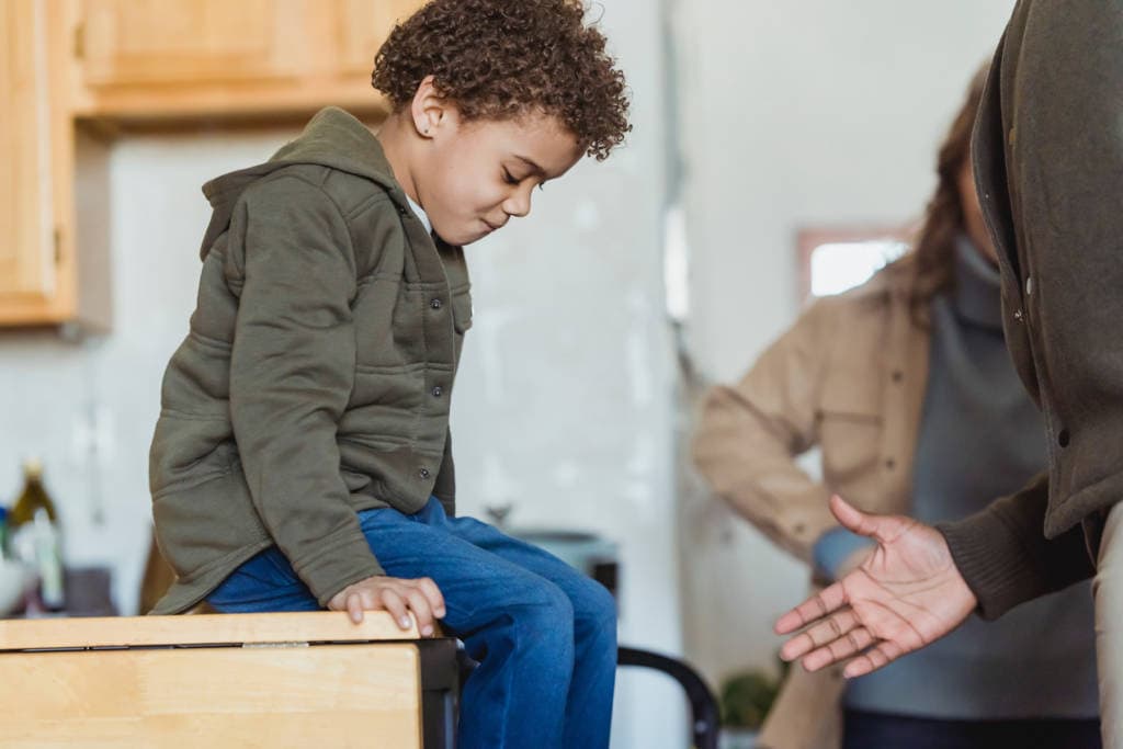six year old biracial boy sitting on kitchen counter being talked to by adult