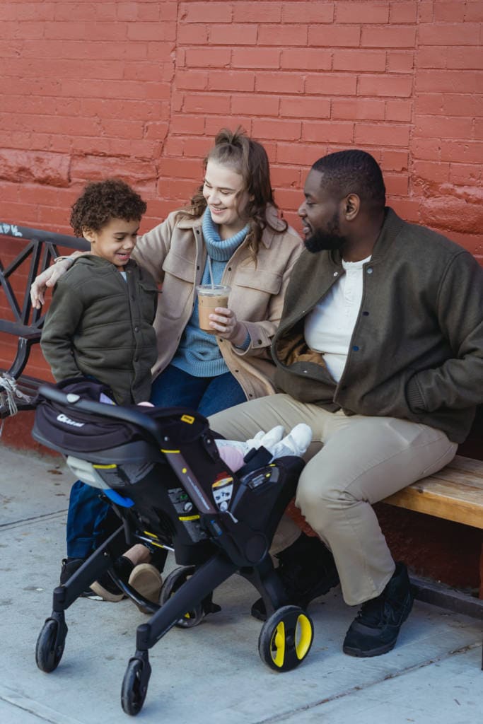 biracial couple on bench with six year old boy and baby in stroller
