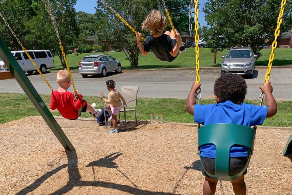 three children, from the back, swinging on swings