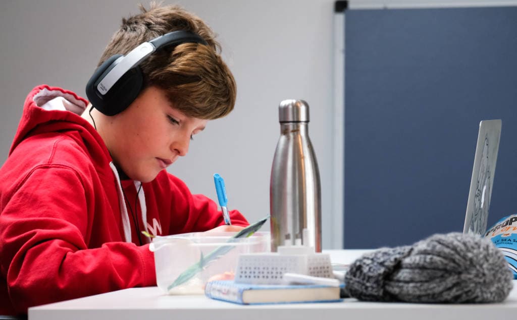 middle school boy wearing headphones doing homework at a table
