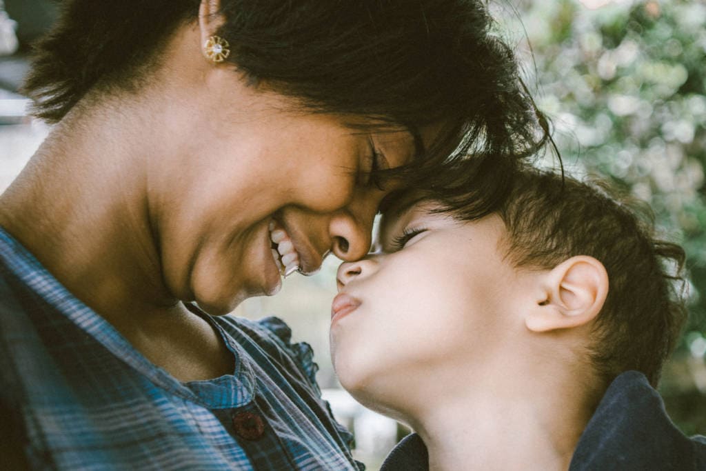 black mother touching noses with small boy and smiling