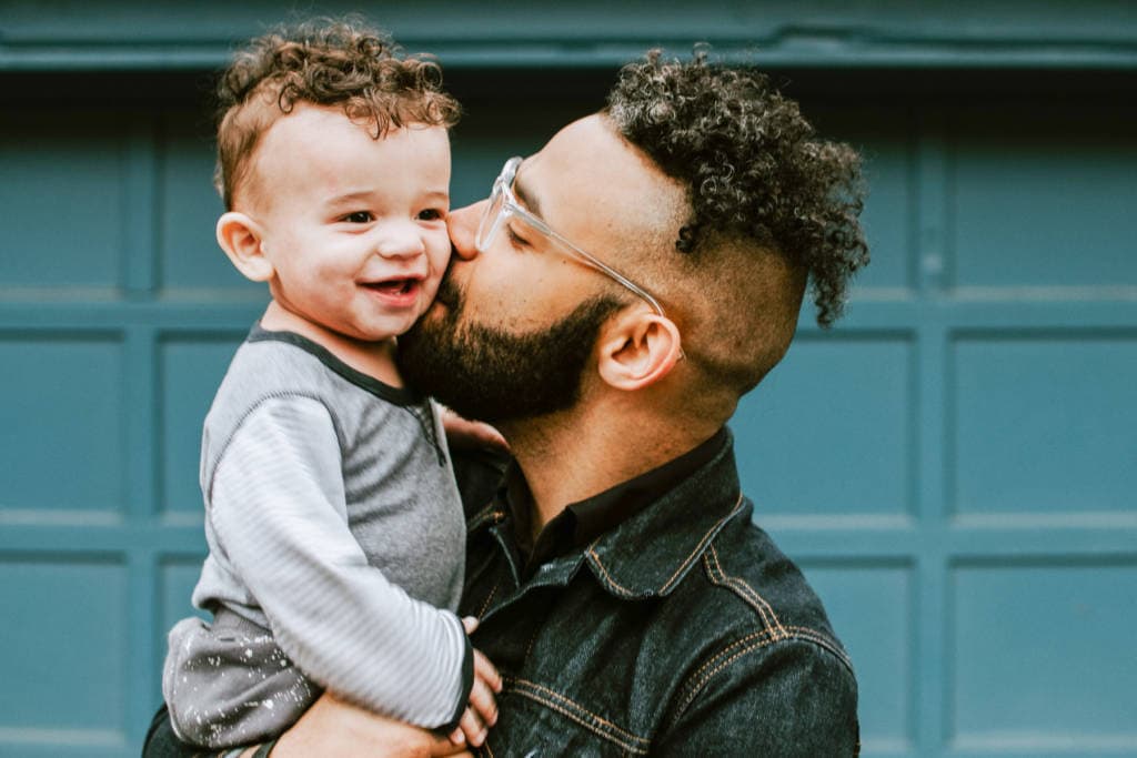dad holding young boy kissing him on cheek