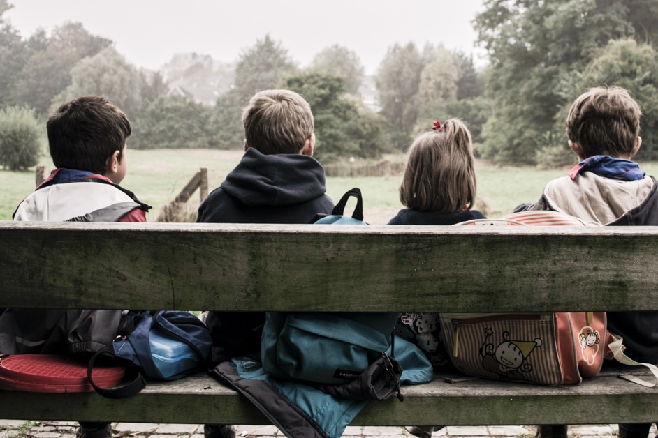 back of four children sitting on a bench on a dreary day
