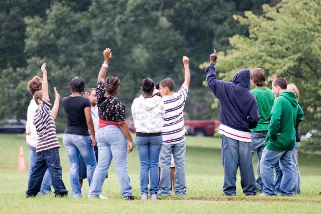 group of teens stand in field hands raised, facing away from camera