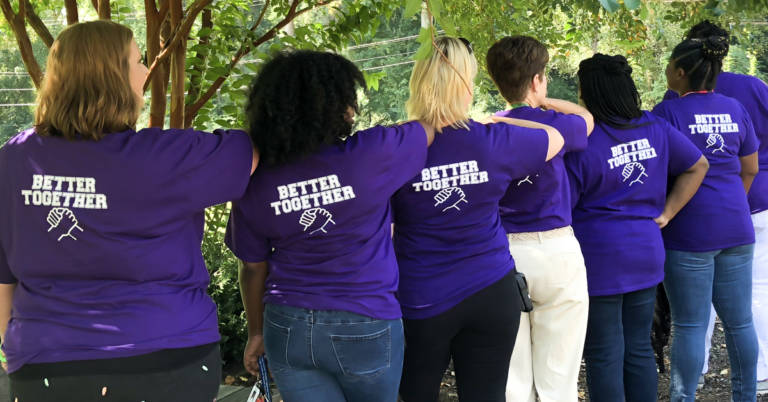 line of teachers standing in a row backs to camera. shirts say "better together"