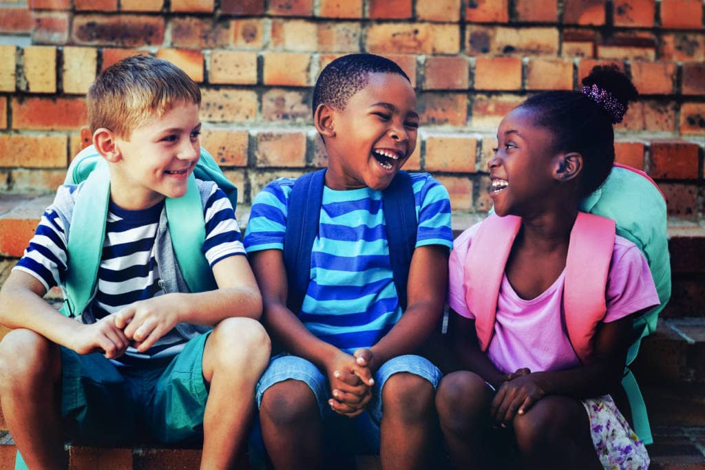 three children with bookbags sitting on steps laughing