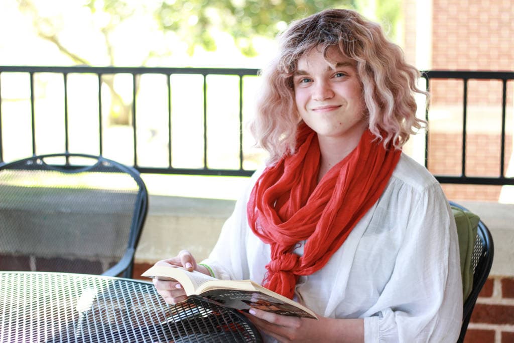 young adult reading on porch wearing white shirt and red scarf