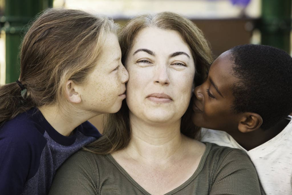 Happy mother being kissed on both sides of face by sons