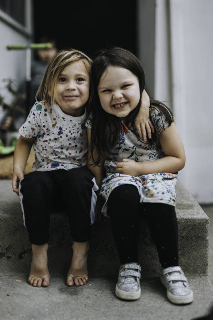 2 young siblings sitting on steps smiling, arms around each other