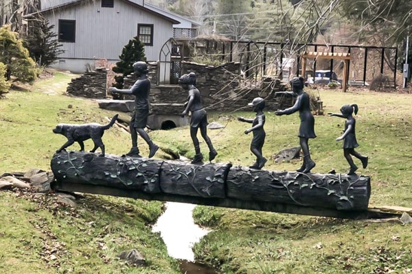 statue of children walking across creek on bridge