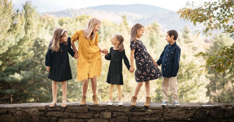 five children standing on a rock wall in front of mountain range