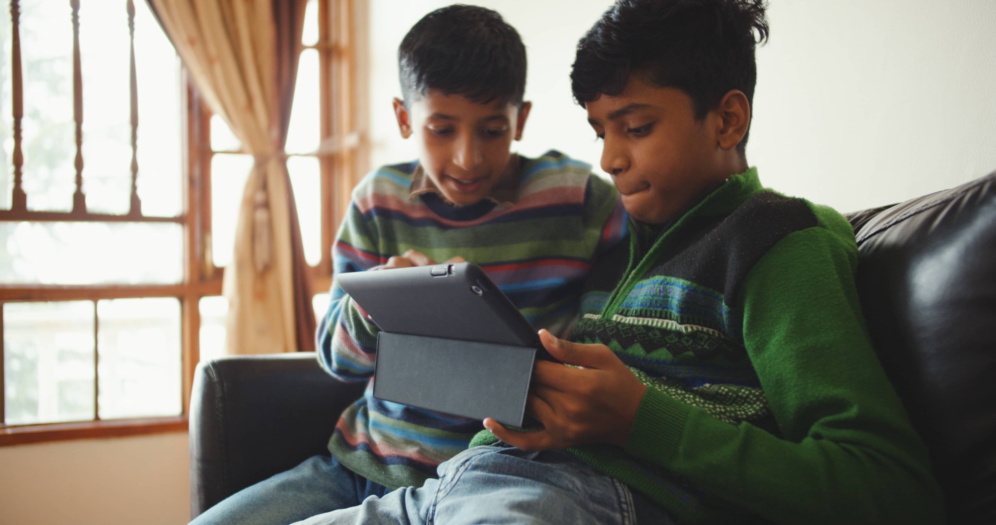 two brothers sitting on a sofa looking at a tablet