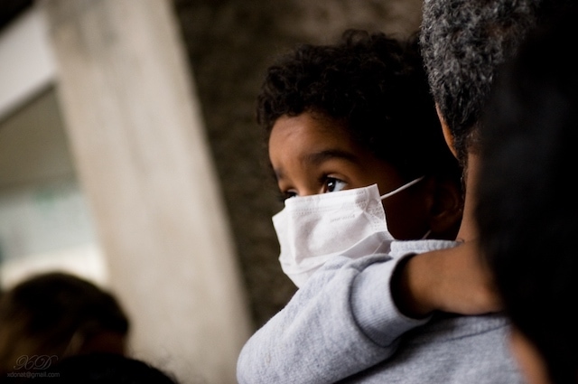 little black boy being held by parent wearing a mask