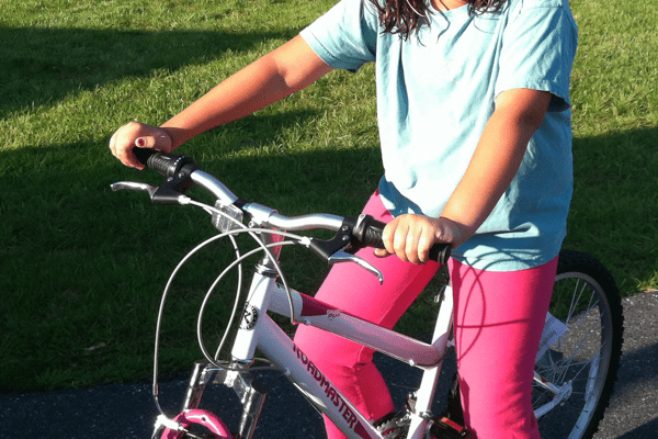 girl wearing pink pants and a light blue shirt sits on a bike, waiting to ride